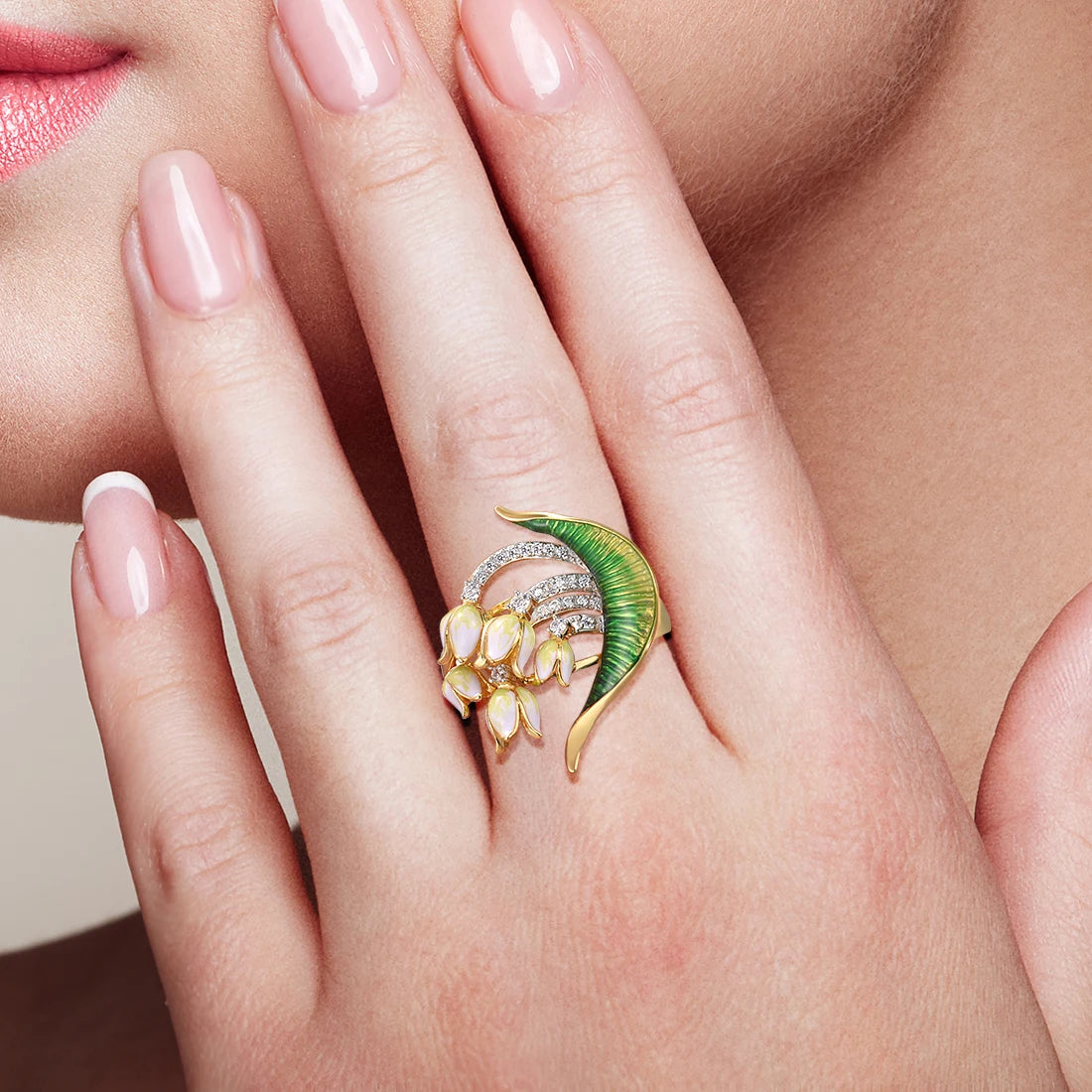 Gold ring featuring a sculpted green enamel leaf, curved pavé-set arcs, and clusters of small pink flower buds