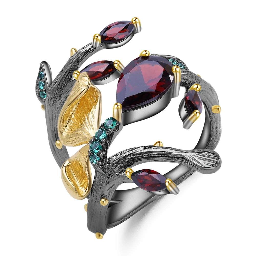 Dark branch-like ring with red marquise and teardrop stones, accented by gold floral elements and small green gems.