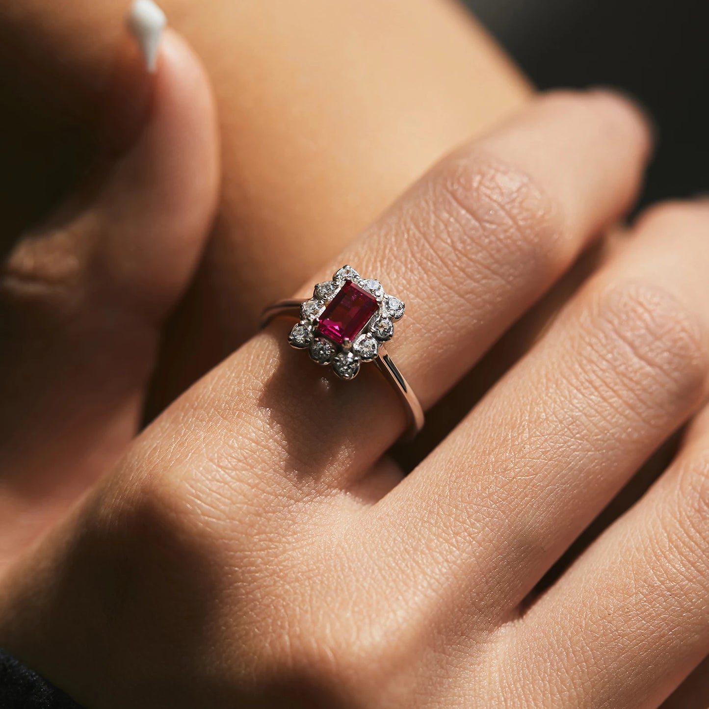 Silver ring with rectangular ruby-pink gemstone surrounded by clear stones in a floral cluster