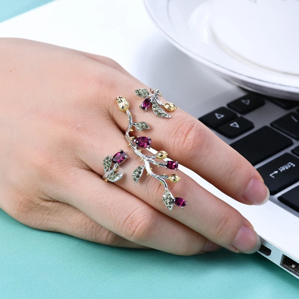 Double-finger ring with branch-like silver bands, deep pink stones, golden buds, and green pavé leaves from the Rossa Collection.