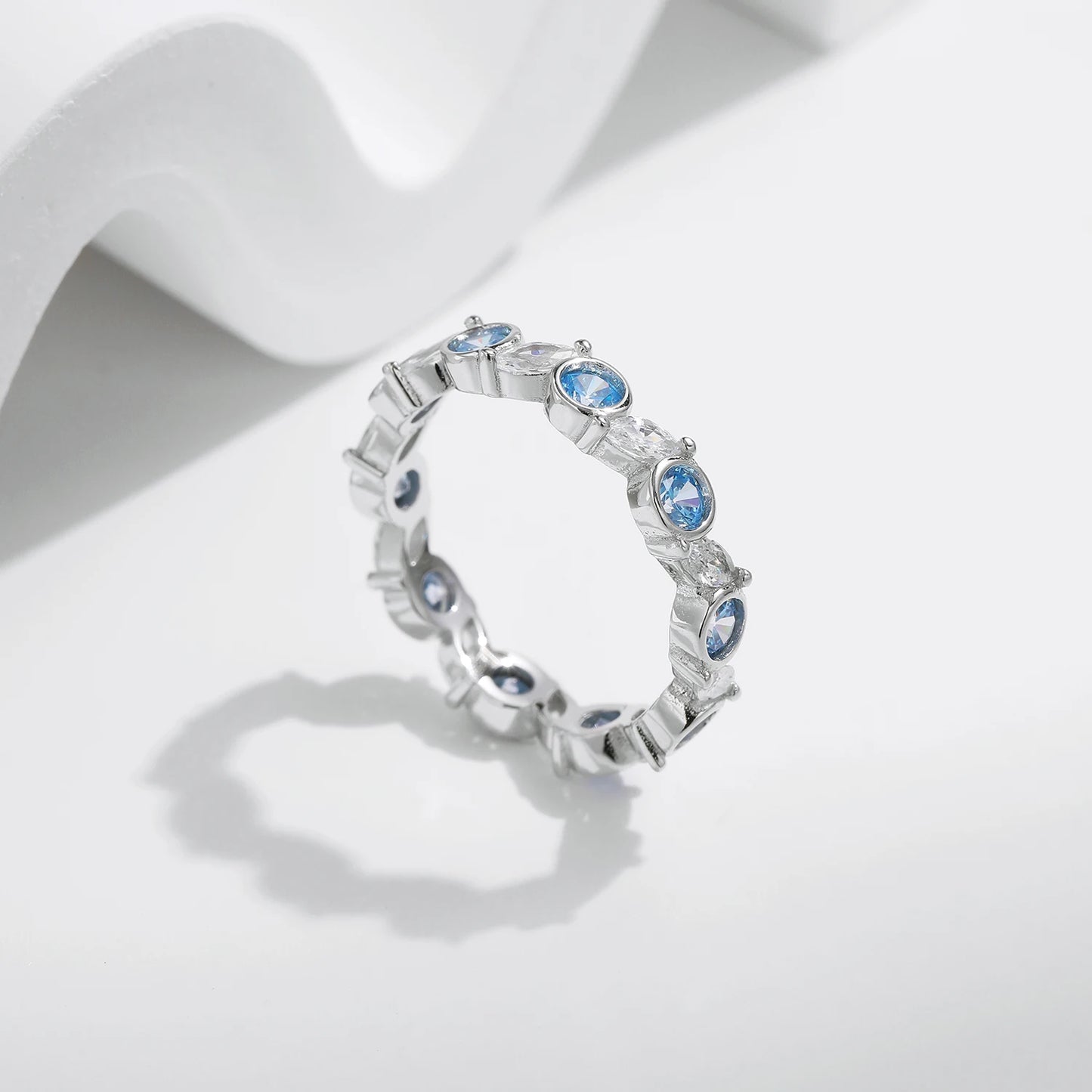 Sterling silver eternity ring with alternating light blue and clear round stones in bezel and prong settings