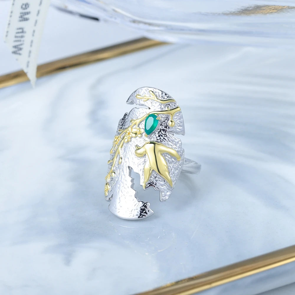 Silver and gold ring with a bird in flight and green gemstone on textured background