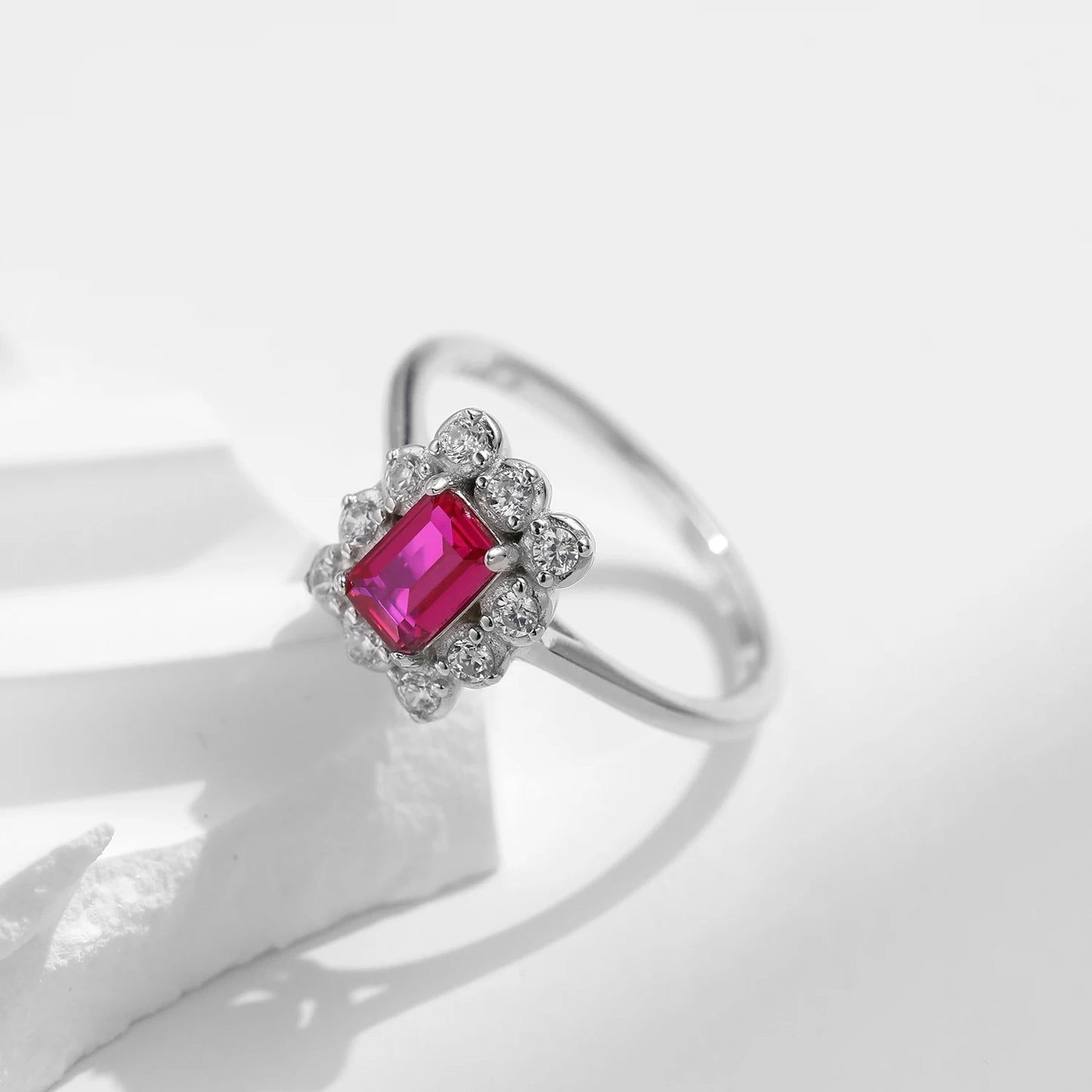Silver ring with rectangular ruby-pink gemstone surrounded by clear stones in a floral cluster