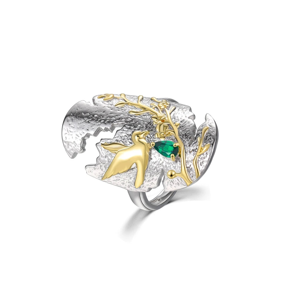 Silver and gold ring with a bird in flight and green gemstone on textured background