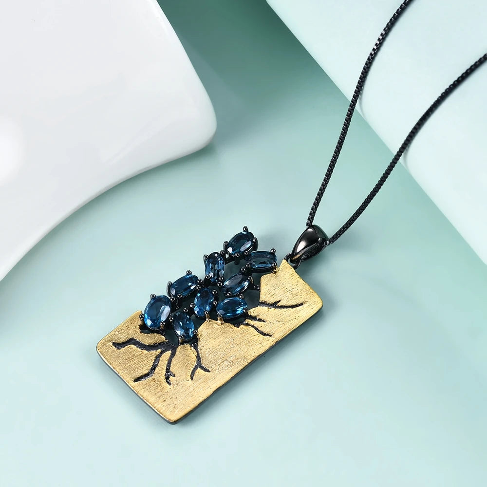 Rectangular gold pendant featuring dark branch-like details set with oval blue gemstones, hanging from a black chain