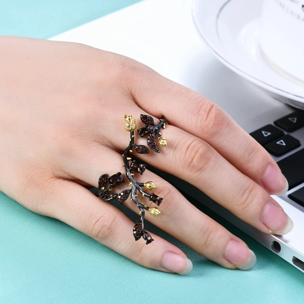 Double-finger black ring shaped like a flowering branch with purple, green, and gold detailing