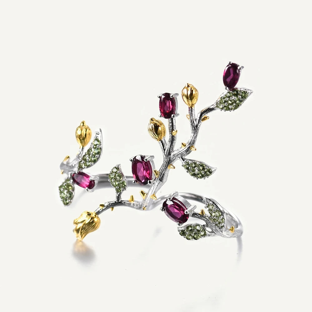 Double-finger ring with branch-like silver bands, deep pink stones, golden buds, and green pavé leaves from the Rossa Collection.