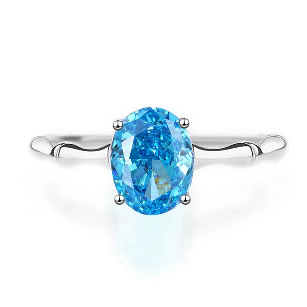 Silver ring with a vivid oval-cut blue gemstone set in a simple band, displayed on a light blue background