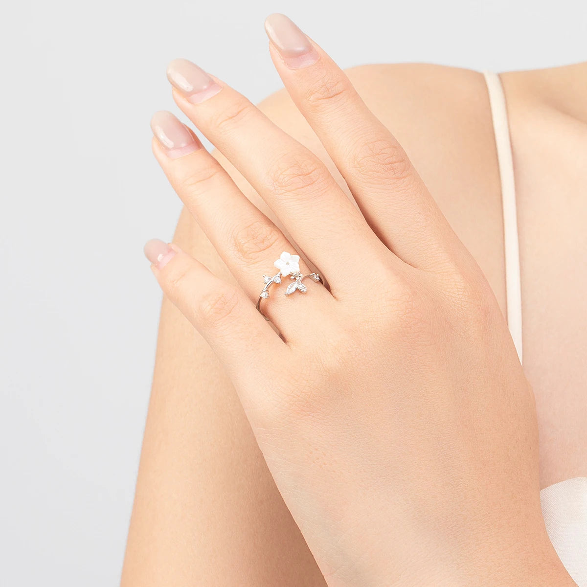 Delicate silver ring featuring a white carved flower and sparkling leaf-shaped stones arranged in a graceful, curved design.