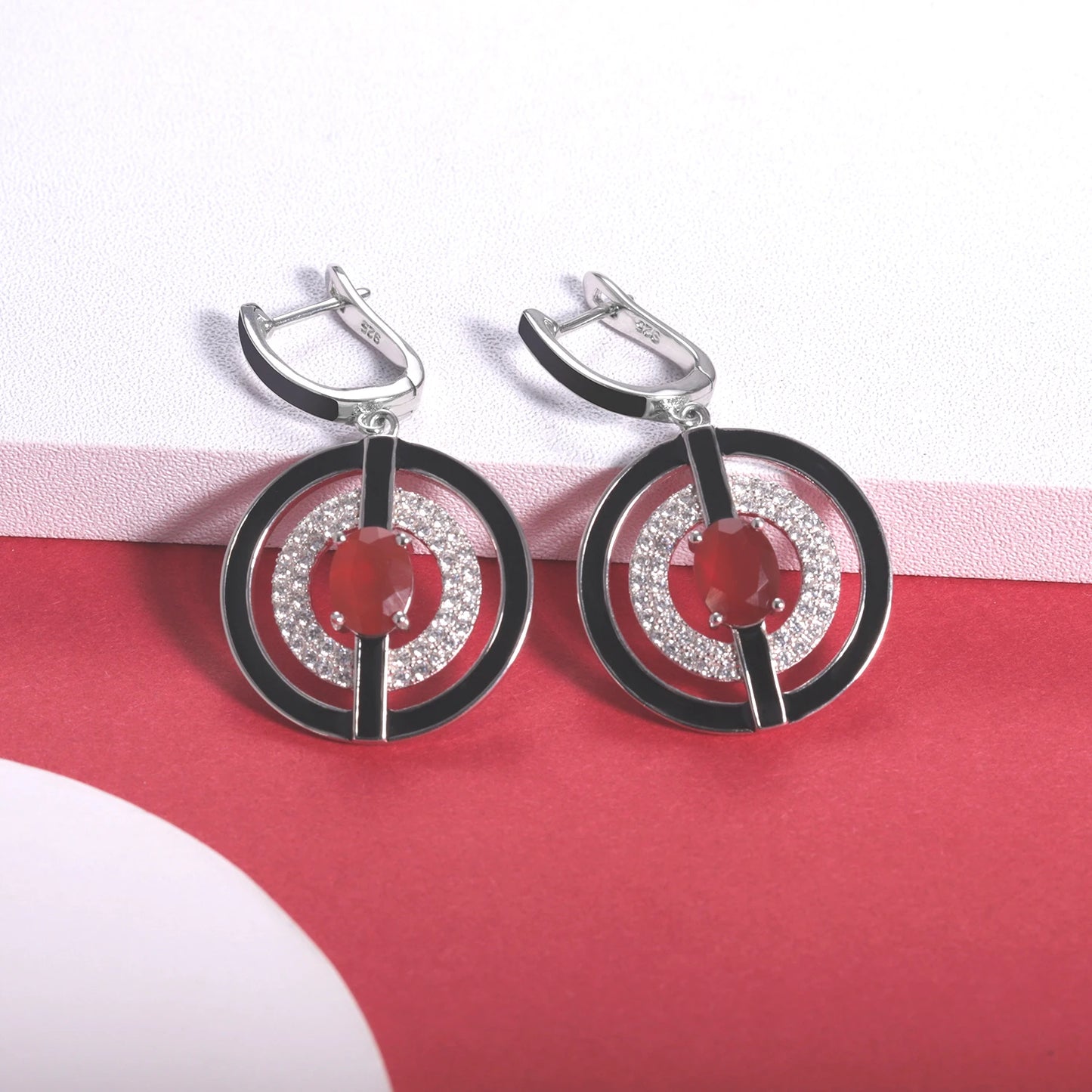 Sterling silver earrings with black enamel rings, pavé-set stones, and central red oval gems, from the Obliqua design.