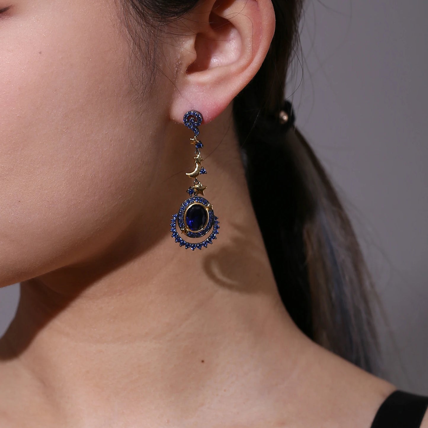 Dangling earrings with gold moon and star charms, deep blue oval stones, and pavé-set blue crystals in a celestial design