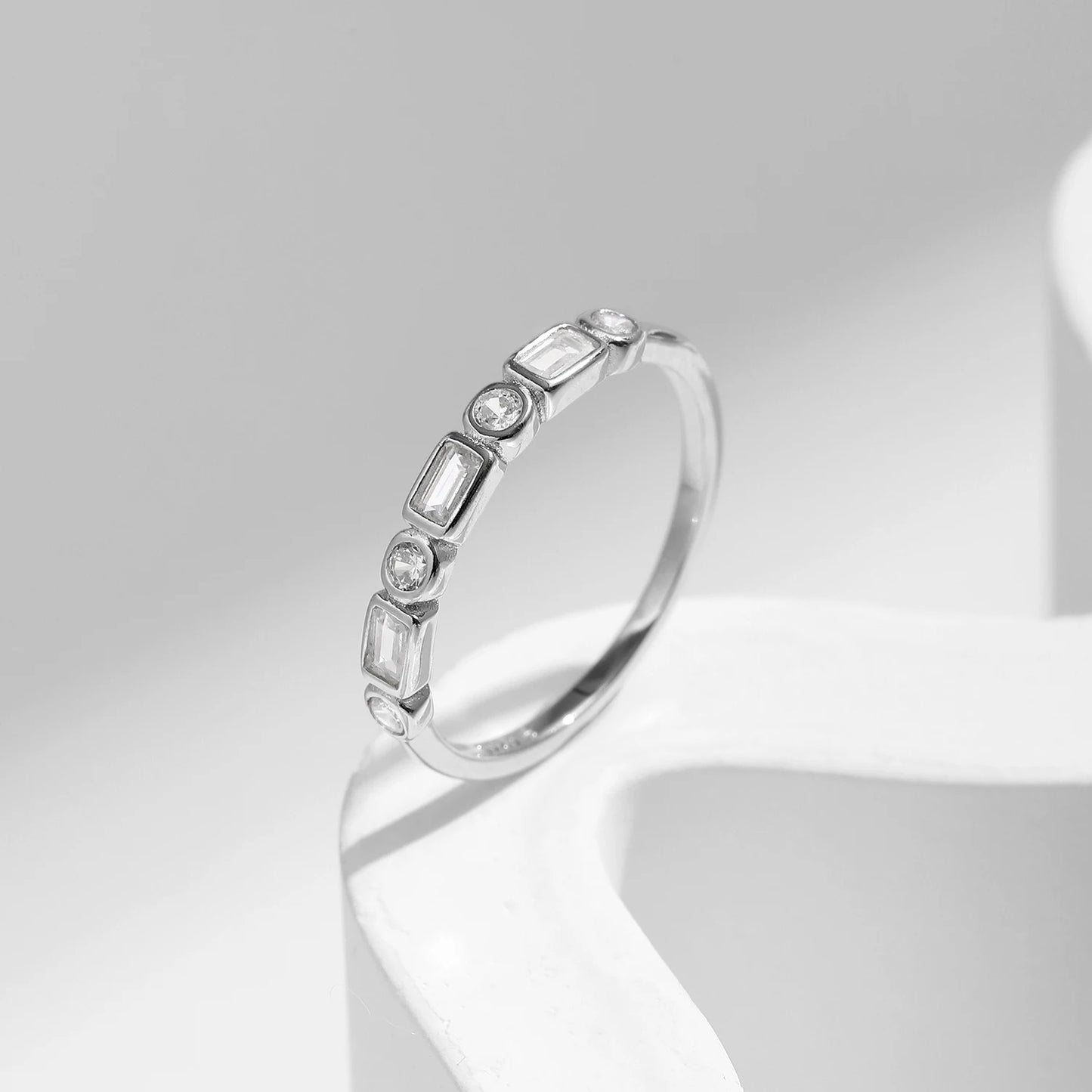Silver ring featuring alternating round and baguette-cut white stones in a half-band setting.