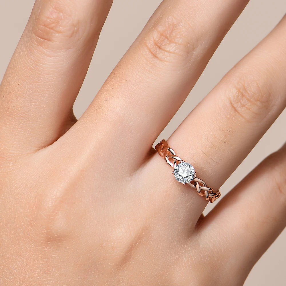 Gold ring with a braided band design and a round-cut clear central stone in a four-prong setting.