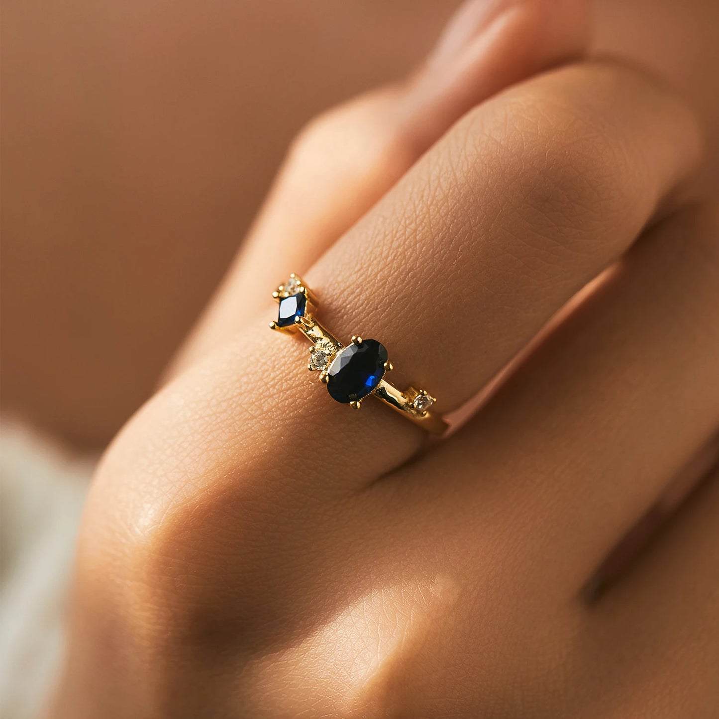 Gold-plated ring with deep blue oval and round stones set in a modern scattered design