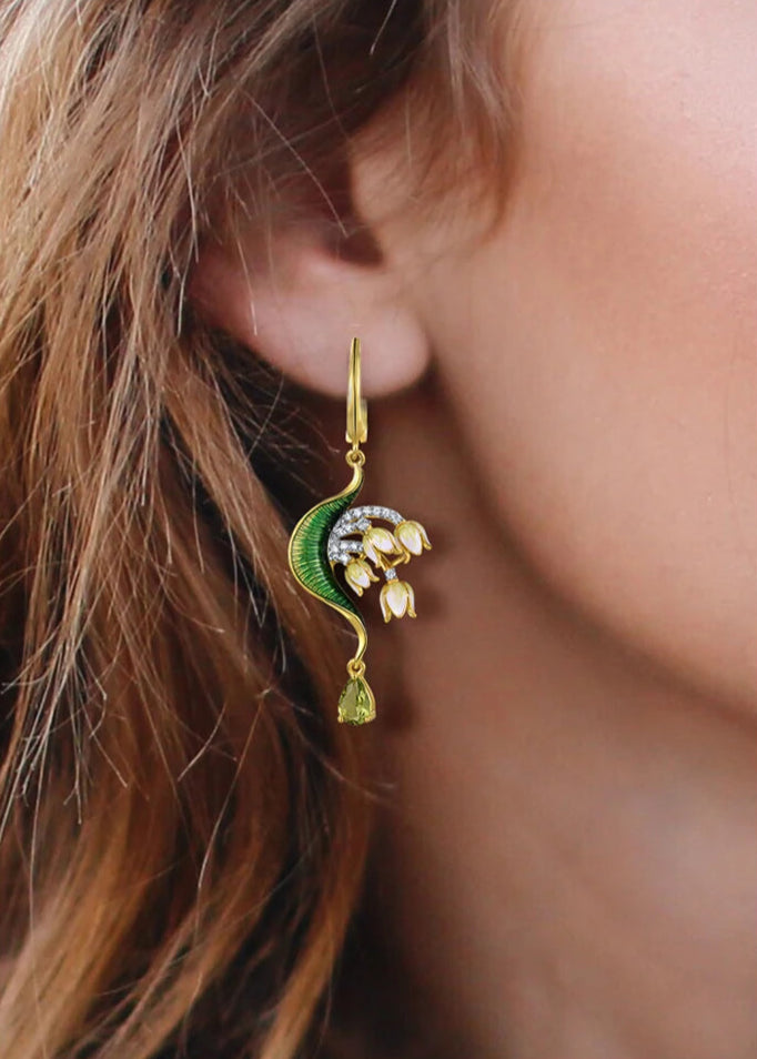 Close-up of a nature-inspired jewelry set featuring a green enameled leaf design with white and yellow floral elements, accented with sparkling stones and gold detailing.