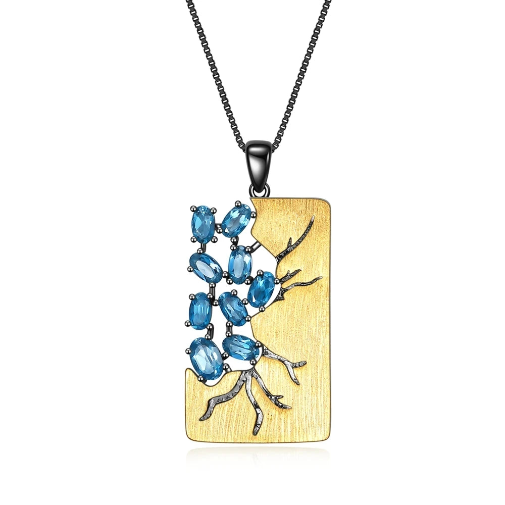 Rectangular gold pendant featuring dark branch-like details set with oval blue gemstones, hanging from a black chain