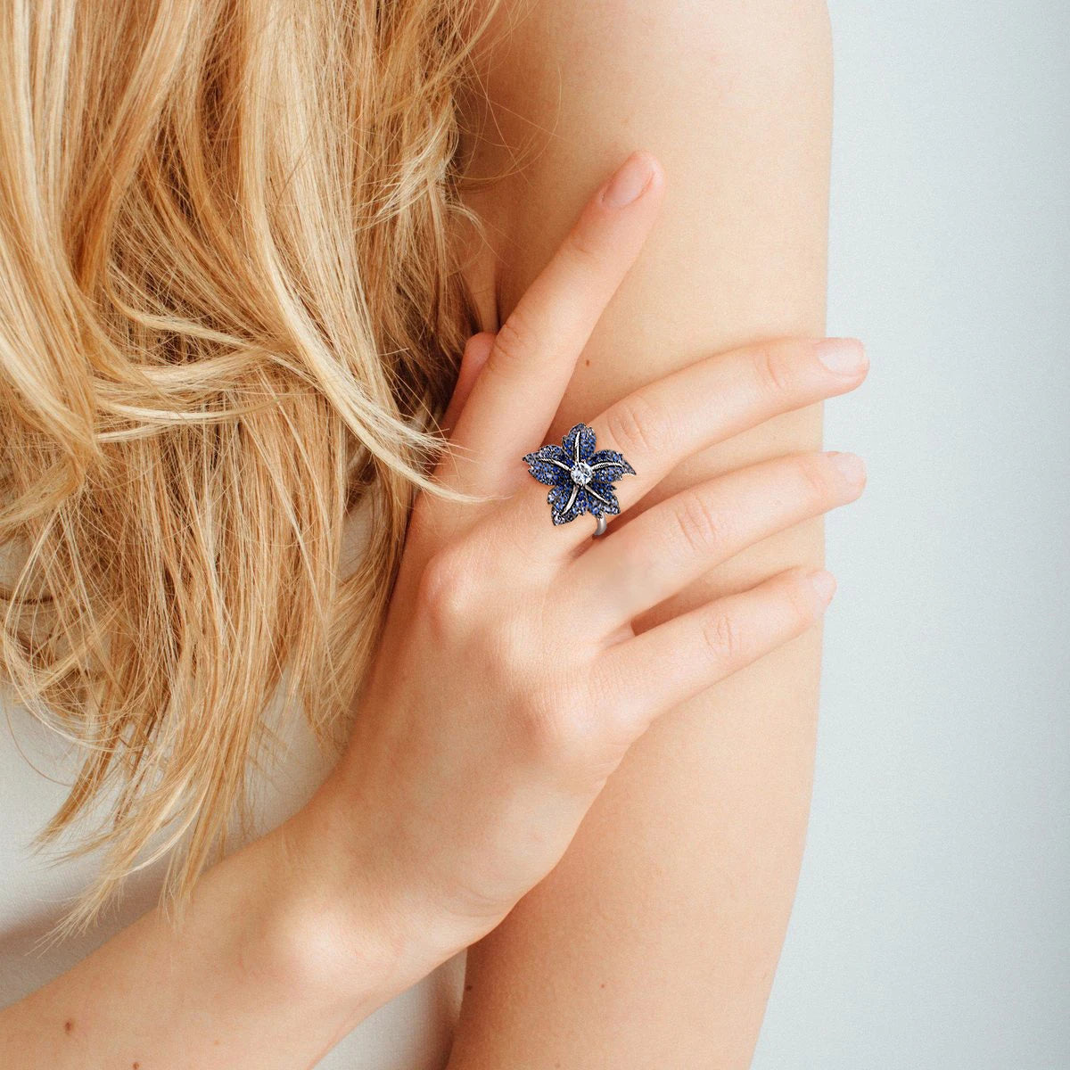 Silver ring shaped like a flower, with deep blue pavé stones and a clear central gem