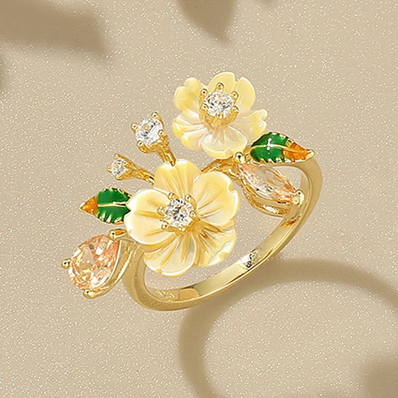 Yellow flower ring with gemstone accents and green enamel leaves on gold band