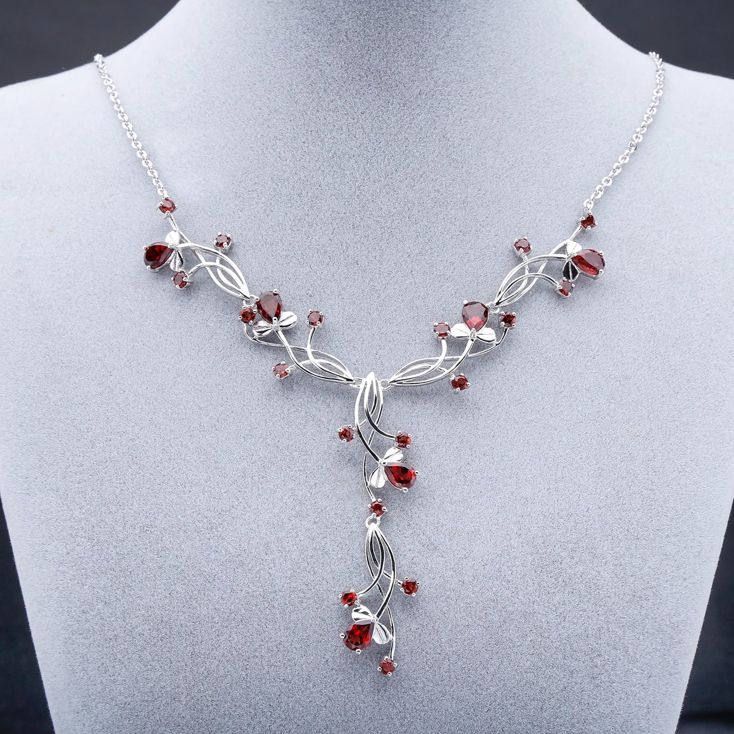 Silver necklace with a swirling vine-like structure, adorned with deep red gemstones arranged in floral and geometric clusters.