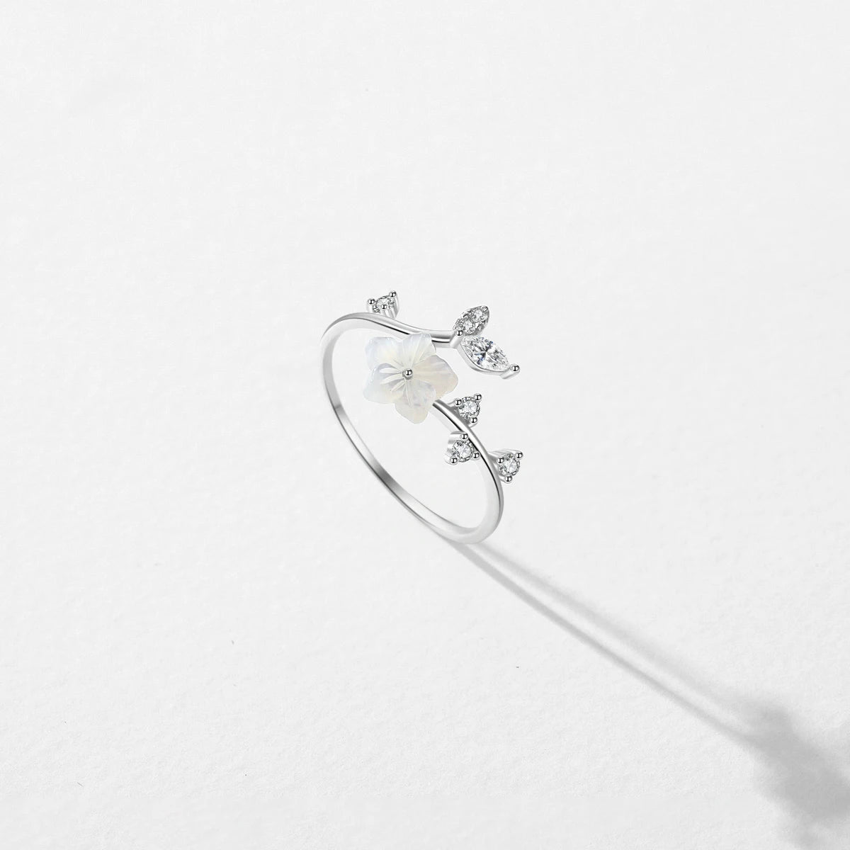 Delicate silver ring featuring a white carved flower and sparkling leaf-shaped stones arranged in a graceful, curved design.