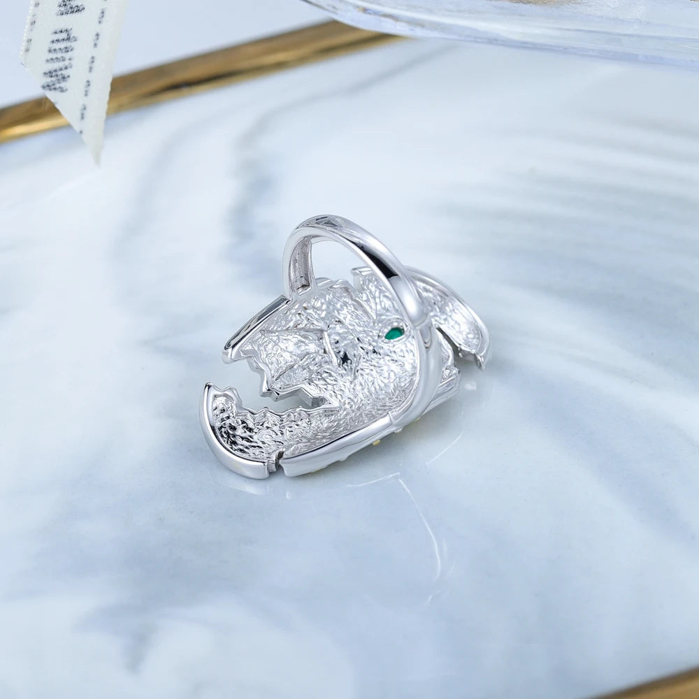 Silver and gold ring with a bird in flight and green gemstone on textured background