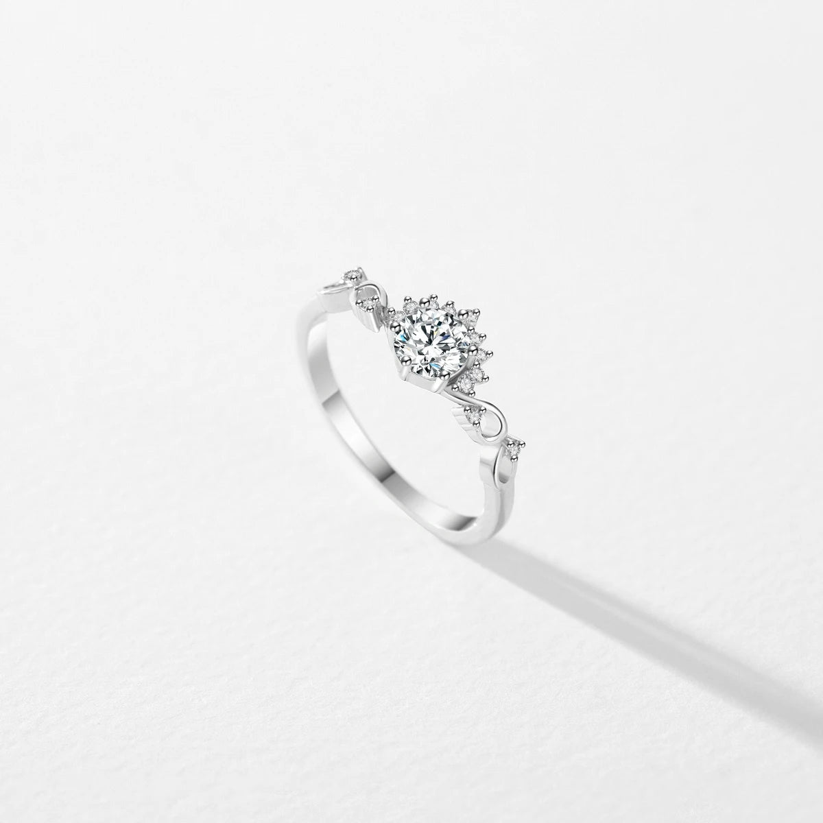 Silver ring with a central round-cut stone surrounded by delicate side diamonds and twisted vine-like detailing.