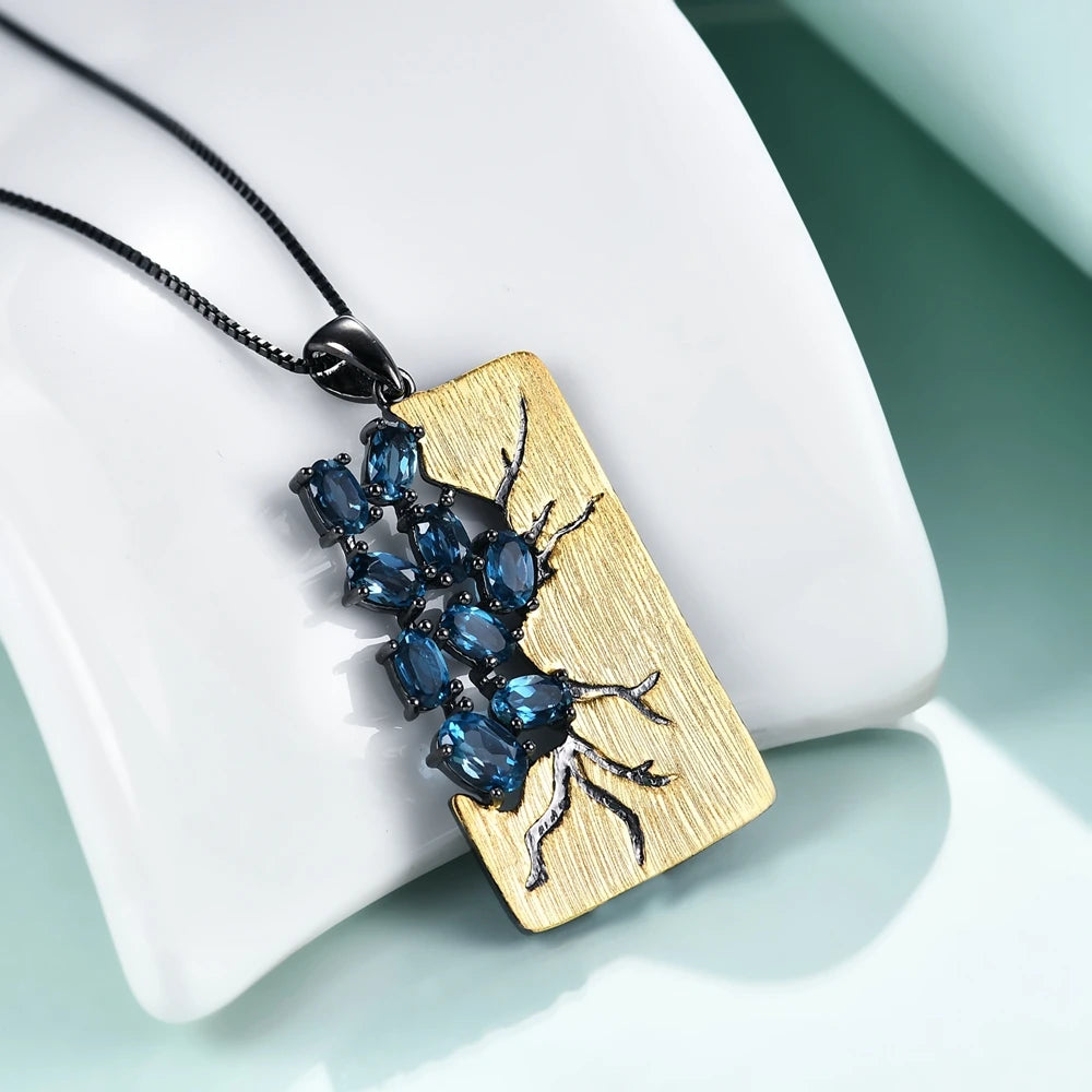 Rectangular gold pendant featuring dark branch-like details set with oval blue gemstones, hanging from a black chain
