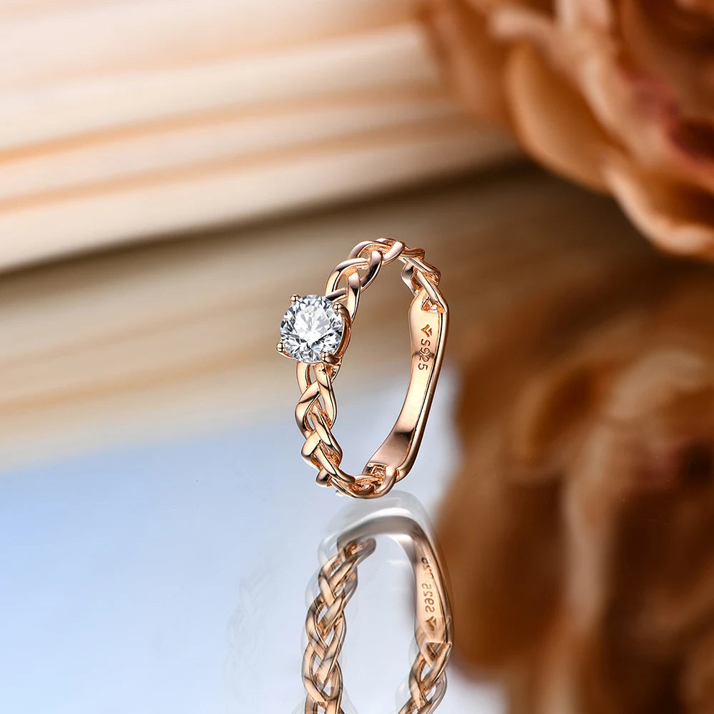 Gold ring with a braided band design and a round-cut clear central stone in a four-prong setting.