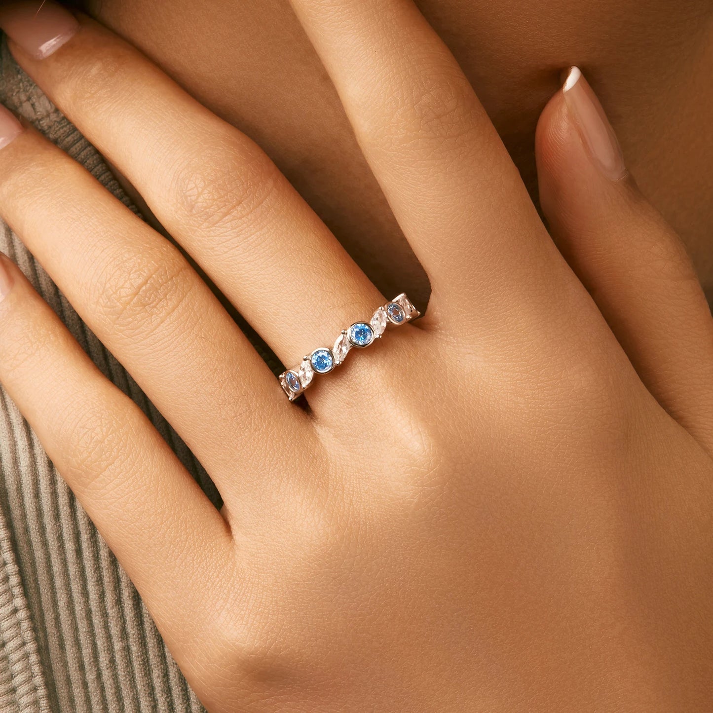 Sterling silver eternity ring with alternating light blue and clear round stones in bezel and prong settings