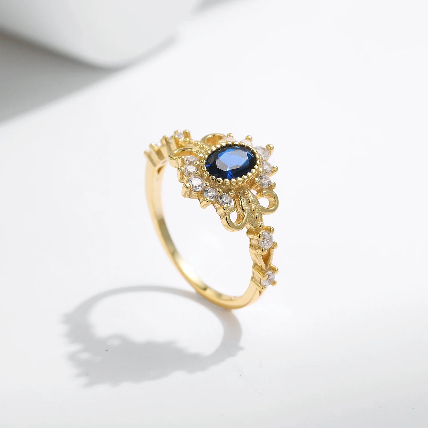 Vintage-style gold ring with deep blue oval center stone surrounded by clear accent stones