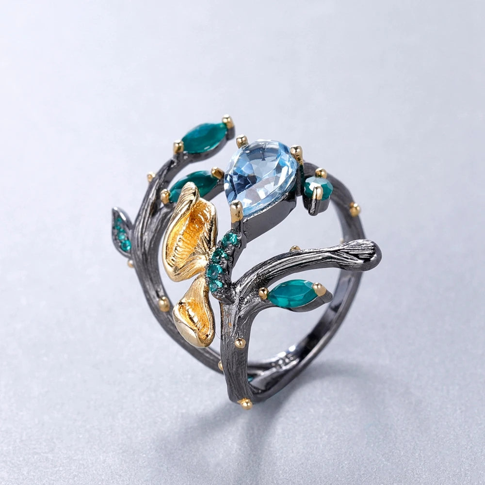 Black branch-style ring with sky-blue and green stones, gold leaves, and textured detailing