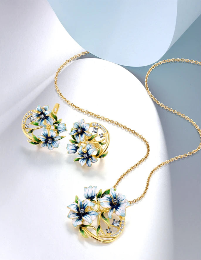 Gold floral jewelry set with white and blue enamel blossoms, green leaves, and delicate cubic zirconia curves