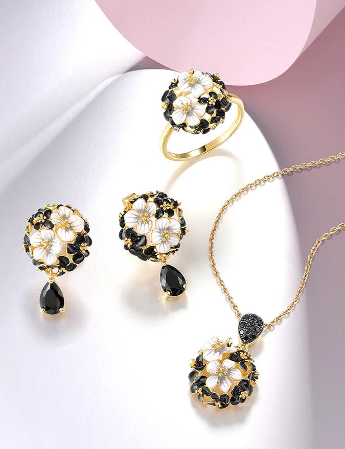 Matching jewelry set featuring black and white floral designs with gold settings, including earrings, pendant, and ring, titled Jacobaeus.