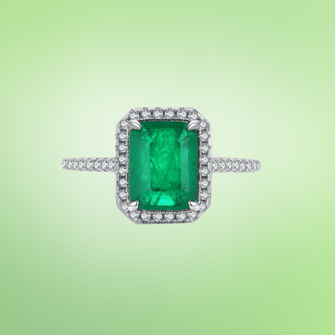 Rectangular green gemstone ring with a halo of clear stones on a silver band.