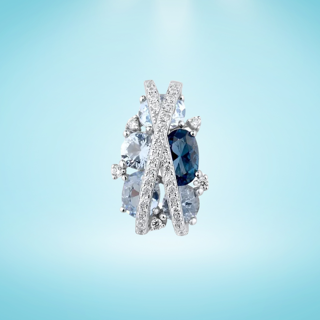 Sterling silver jewelry piece featuring crisscross pavé bands over clustered light and dark blue gemstones, on a light blue background
