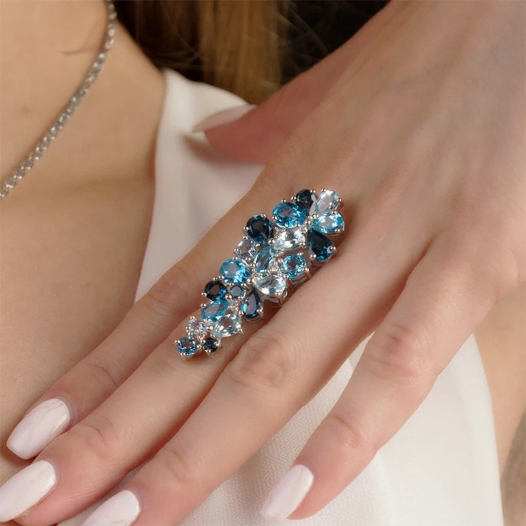 Sterling silver ring adorned with clusters of pear-cut and round-cut blue topaz gemstones in varying shades.
