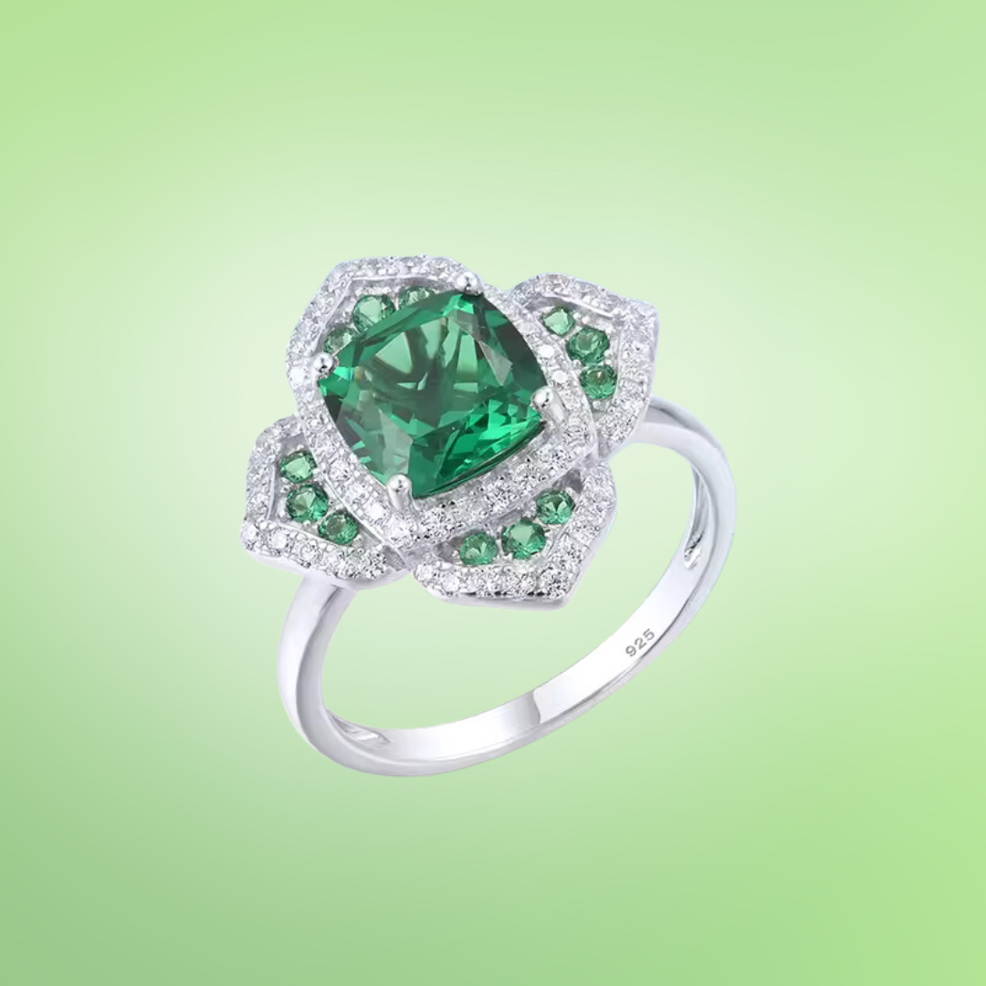 Silver ring with a large cushion-cut green center stone, surrounded by pavé-set crystals in a layered floral-inspired setting