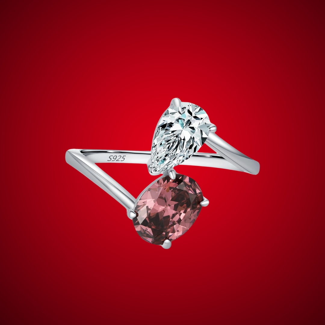Silver ring with a split band featuring a clear pear-cut stone and a deep rose oval gem, shown on a red background from the Rossa collection.