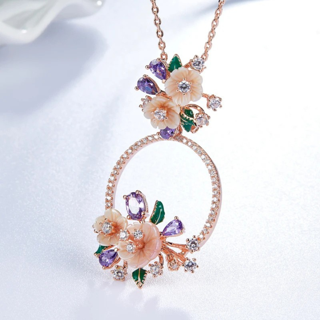 Infiorescenza necklace with a circular pendant adorned with peach flowers, violet gemstones, green enamel leaves, and sparkling white accents.