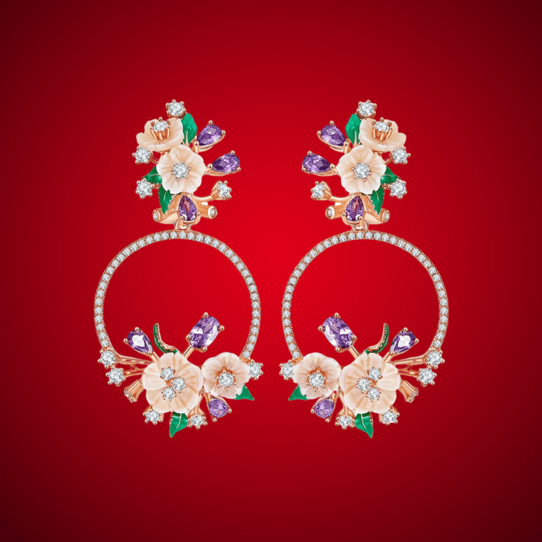 Infiorescenza hoop earrings featuring peach-toned flowers, purple and white stones, and green enamel leaves in an ornate floral arrangement.