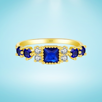 Gold-plated sterling silver ring with a central square-cut deep blue stone and surrounding clear round stones

