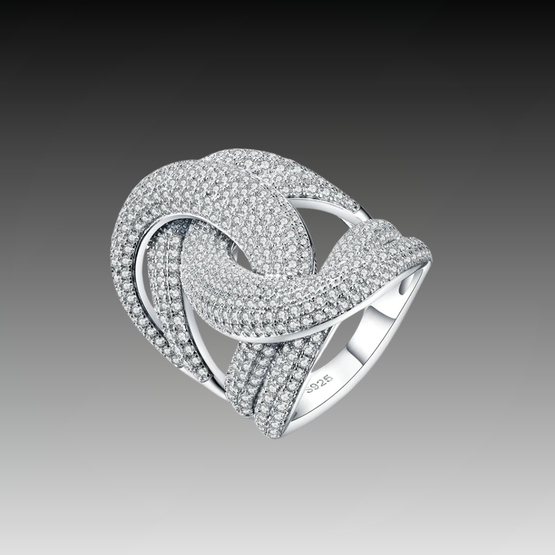 Wide silver ring with interlocking ribbon-like loops, entirely paved with sparkling white stones.


