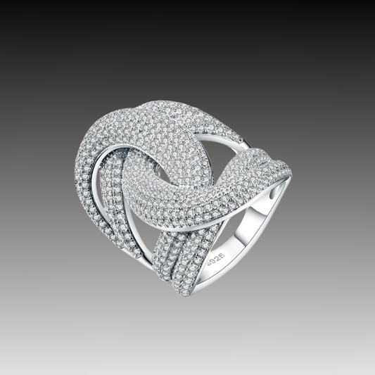 Wide silver ring with interlocking ribbon-like loops, entirely paved with sparkling white stones.

