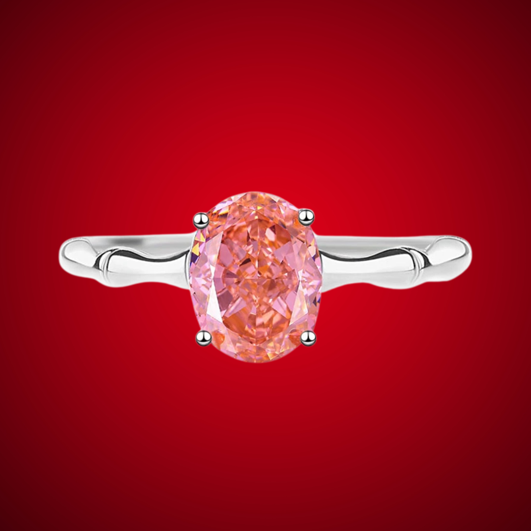 Silver band ring with an oval-cut pink-orange tourmaline stone, displayed against a deep red background from the Rossa collection.

