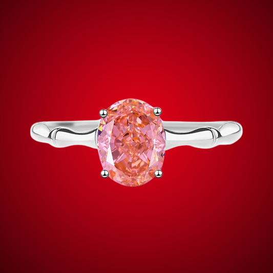Silver band ring with an oval-cut pink-orange tourmaline stone, displayed against a deep red background from the Rossa collection.

