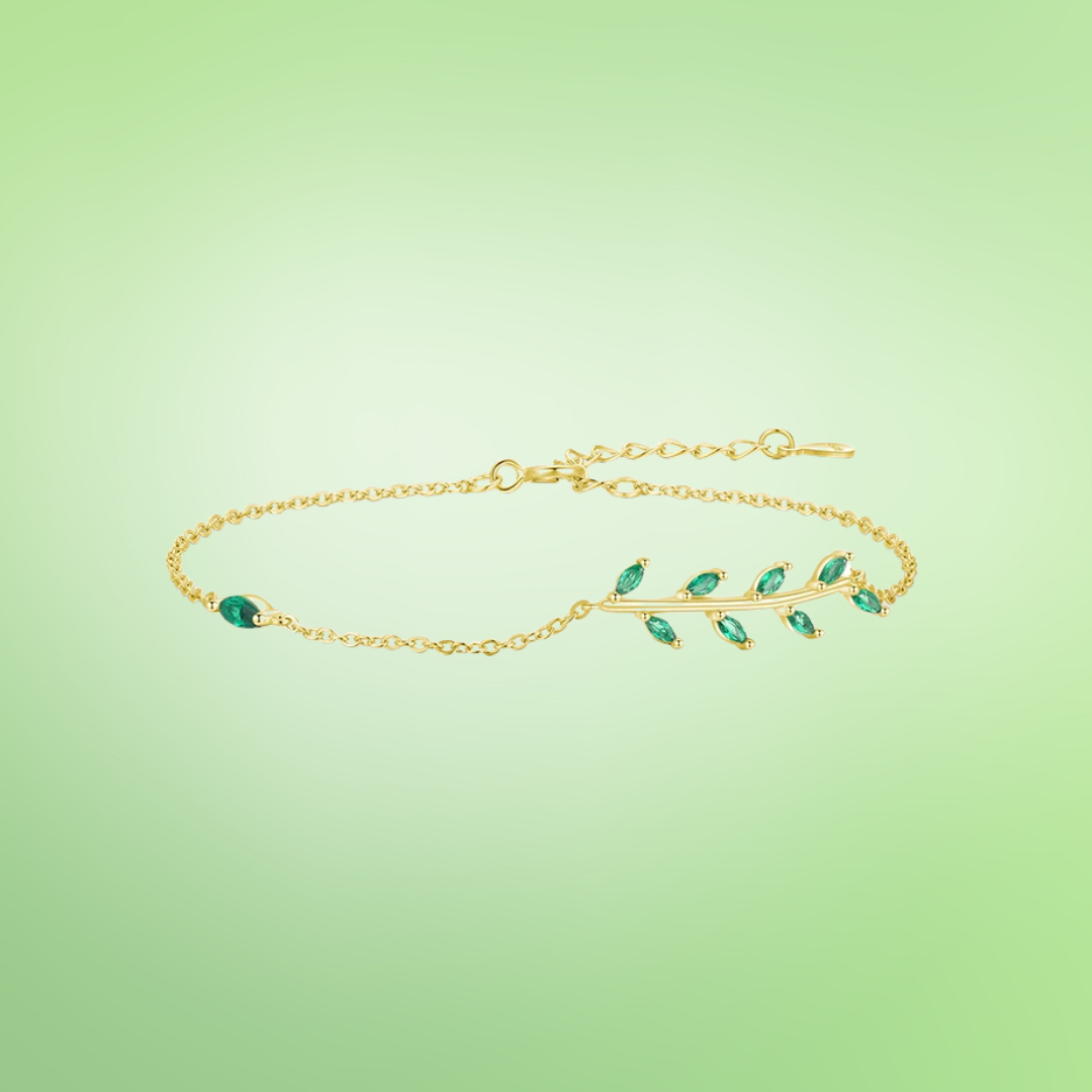 Gold chain bracelet with a delicate green leaf branch design.

