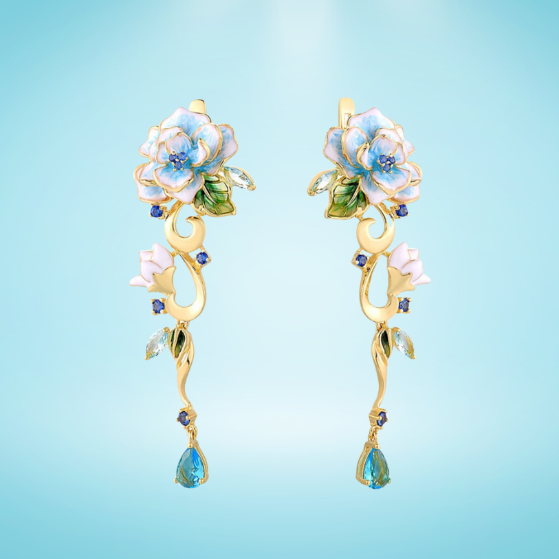 Gold floral earrings with hand-painted white and blue enamel petals, sapphire accents, and dangling blue teardrop stones

