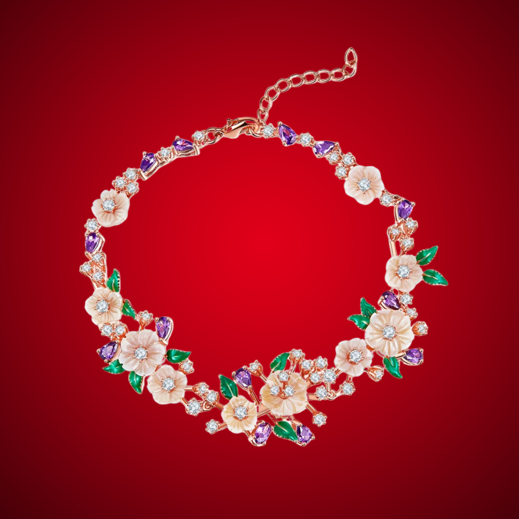 Floral bracelet with soft pink blossoms, green enamel leaves, and purple heart-shaped stones on a rose gold chain, set against a red background.

