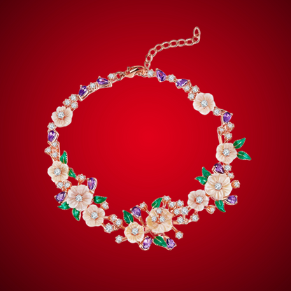 Floral bracelet with soft pink blossoms, green enamel leaves, and purple heart-shaped stones on a rose gold chain, set against a red background.

