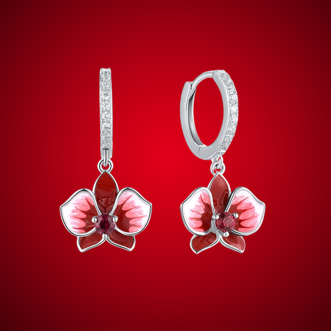 Cuore Rubino earrings featuring red and pink orchid-shaped enamel flowers with sparkling red gemstone centers and crystal-accented hoops.

